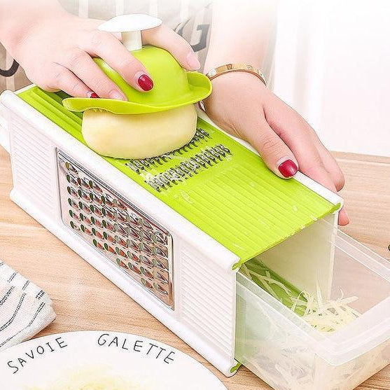 Person using a green and white mandoline slicer to slice vegetables on a wooden surface.