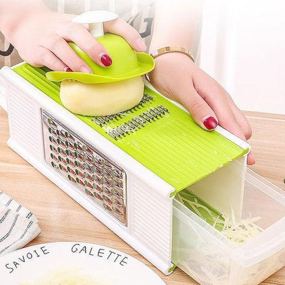 Person using a green and white mandoline slicer to slice vegetables on a wooden surface.
