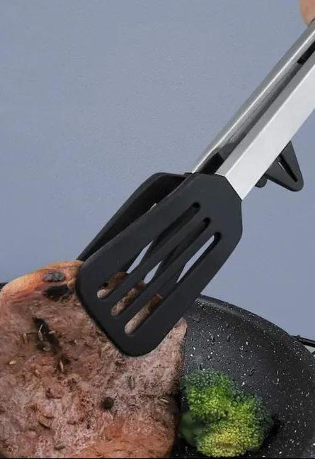 Black spatula with metal handle being used to flip a burger patty on a grill.