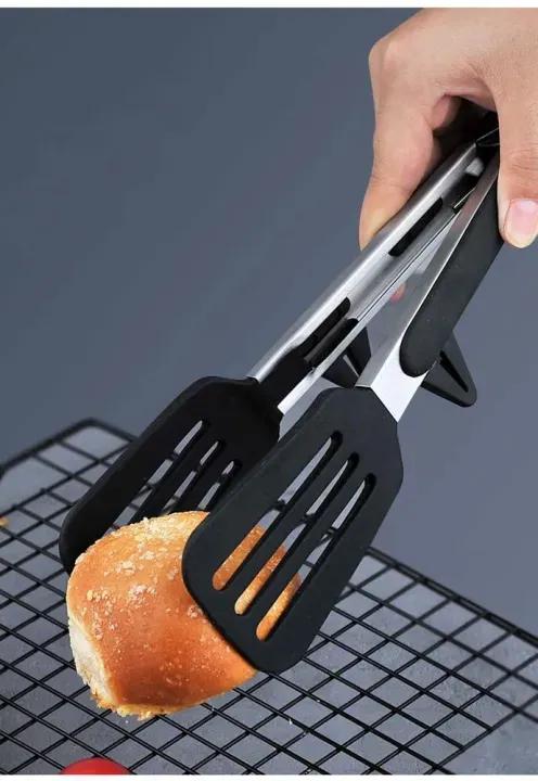 Black and silver kitchen tongs holding a piece of bread on a cooling rack.